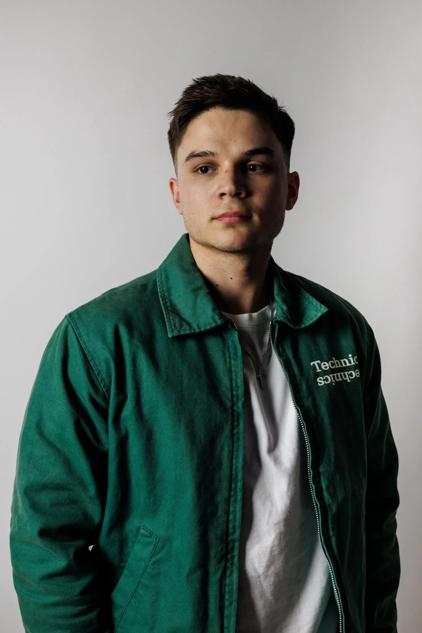 DJ Marian in grüner Jacke mit Technics-Schriftzug vor hellgrauem Studiohintergrund.