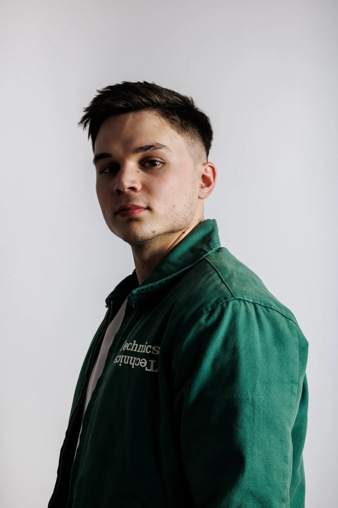 DJ Marian de medio perfil con chaqueta verde con el logo de Technics ante una pared clara.